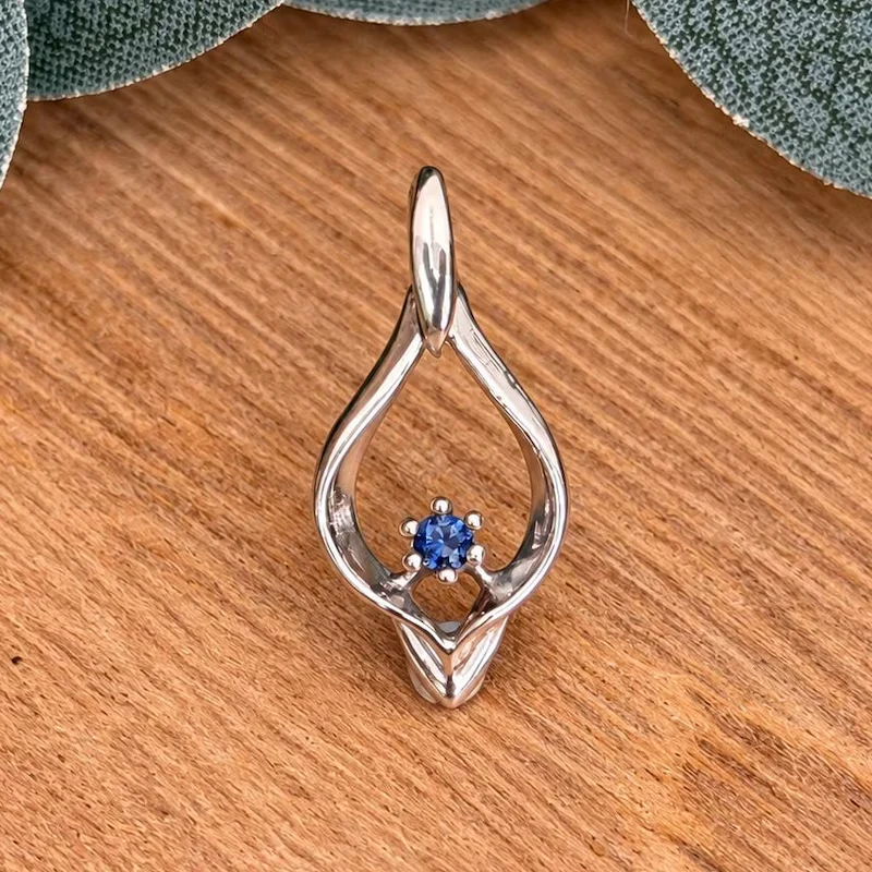 A blue benitoite gemstone in an open teardrop-shaped white gold pendant on wood