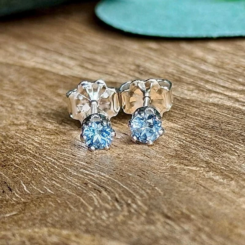 Two pale blue Montana sapphire stud earrings in sterling silver on a wooden surface